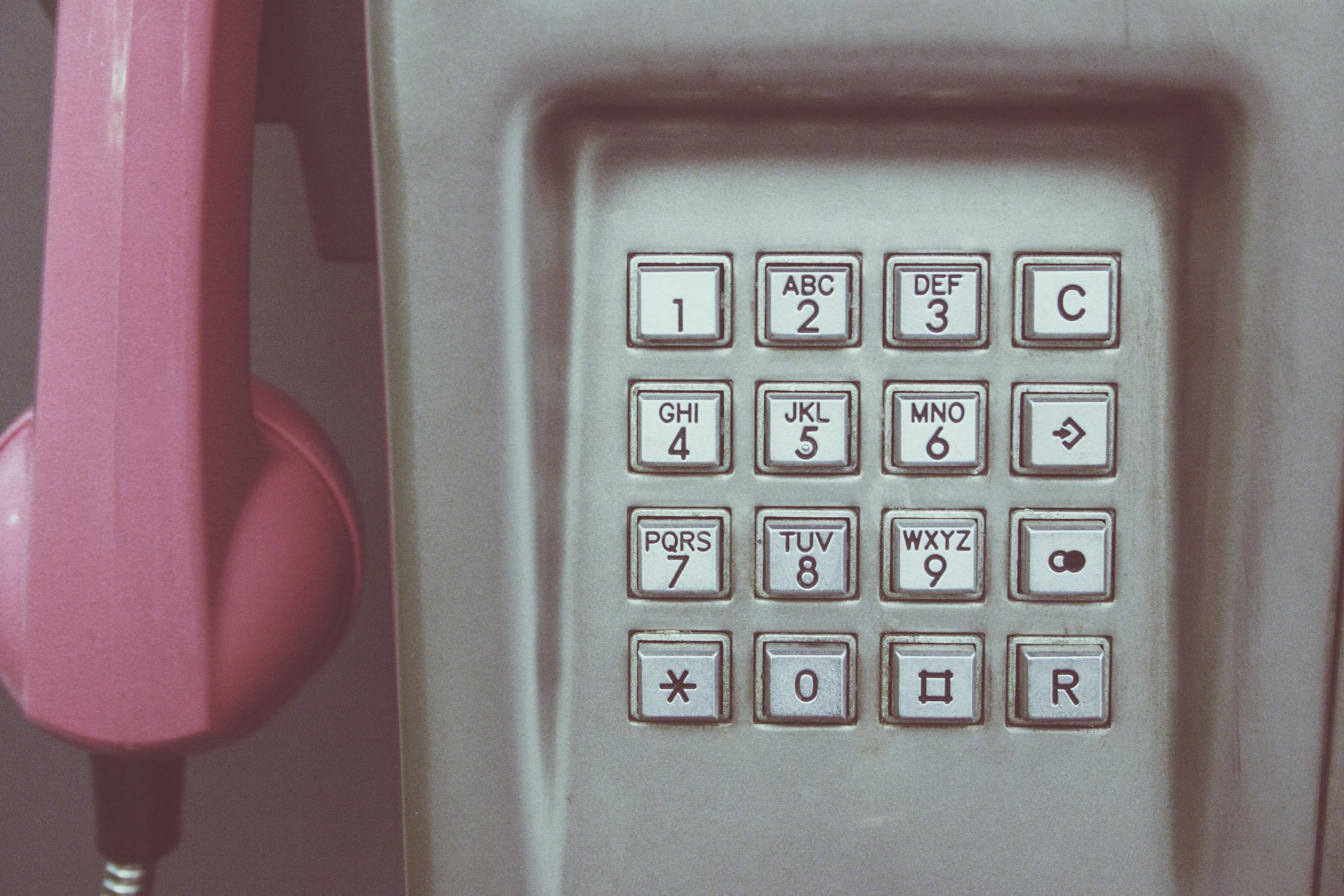 Close-up of a vintage payphone keypad with pink receiver, highlighting retro technology.
