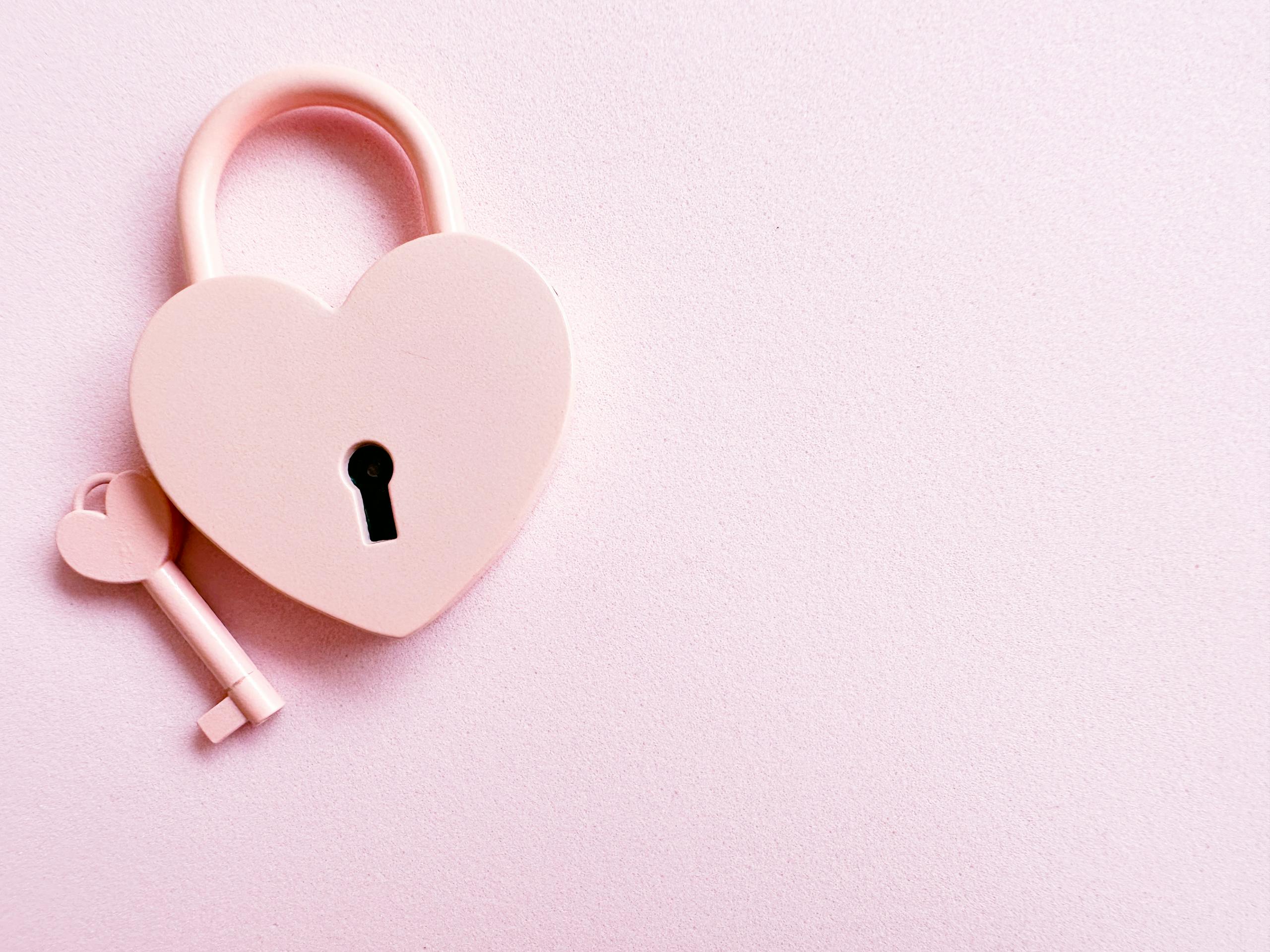 Aesthetic photo of a heart-shaped pink padlock with a matching key on a pink background, perfect for love themes.