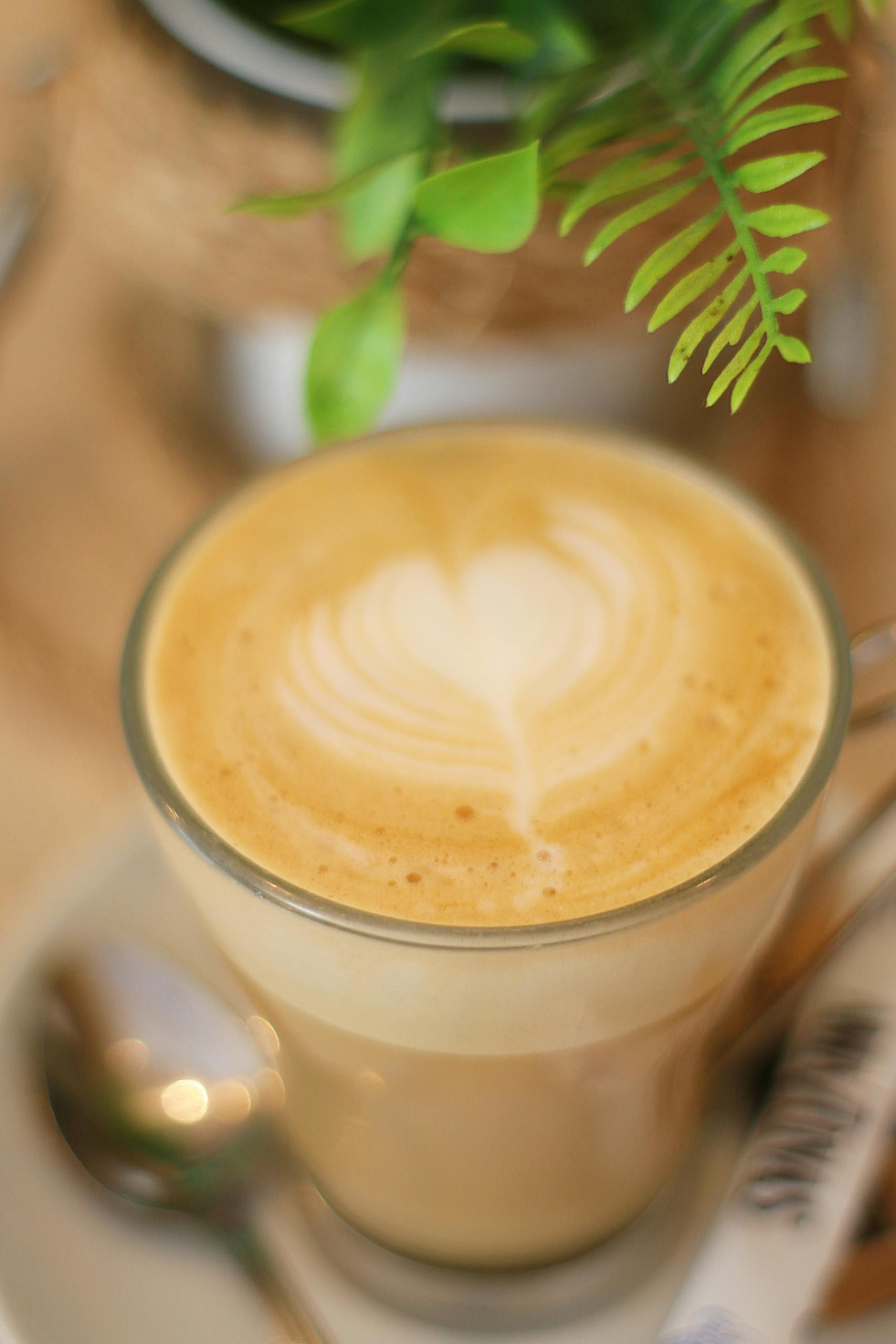 Close-up of a latte with heart-shaped foam art in a glass mug on a saucer.